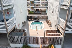 A rooftop pool area with a hot tub, lounge chairs, and a wooden deck.