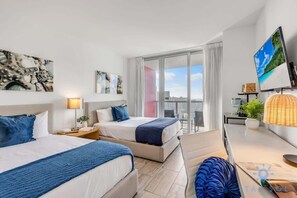 A hotel room with two beds, a TV, a balcony with a view, and artwork on the walls.