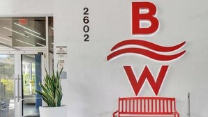 Une entrée d’immeuble avec un banc rouge, une plante en pot et un grand logo rouge et blanc.