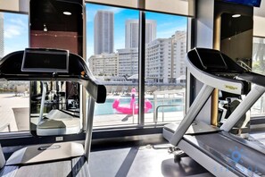 A gym with treadmills and a large window overlooking a pool and city buildings. - Upper studio|Balcony | Pool + Gym| Near Beach (Hallandale Beach)