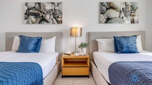 Une chambre d’hôtel avec deux lits, une table de chevet, une lampe et des œuvres d’art accrochées aux murs.