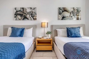 A hotel room with two beds, a nightstand, a lamp, and artwork on the walls. - Upper studio|Balcony | Pool + Gym| Near Beach (Hallandale Beach)