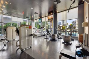A modern gym with various exercise equipment, large windows, and a view of the city.