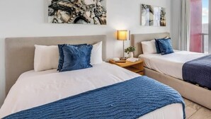 Une chambre d’hôtel avec deux lits, une table de chevet avec une lampe et des œuvres d’art accrochées au mur.