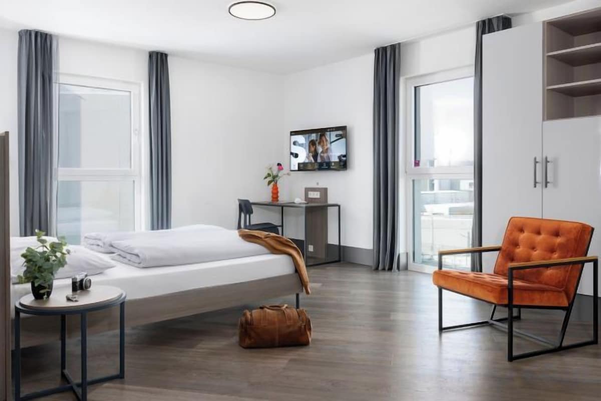 Habitación de hotel moderna con una cama, un escritorio, una silla, un televisor y vistas a la ciudad.