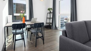 A modern living room with a grey sofa, a wooden dining table with four chairs, a laptop, and a potted plant. - smartments Frankfurt City-Ost (Frankfurt)