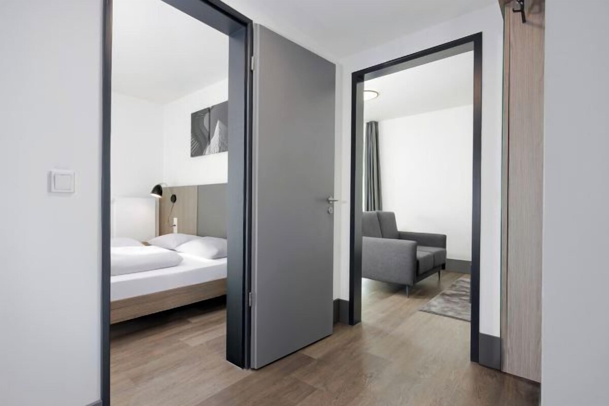 Une chambre moderne avec un lit, un canapé gris et un grand miroir.