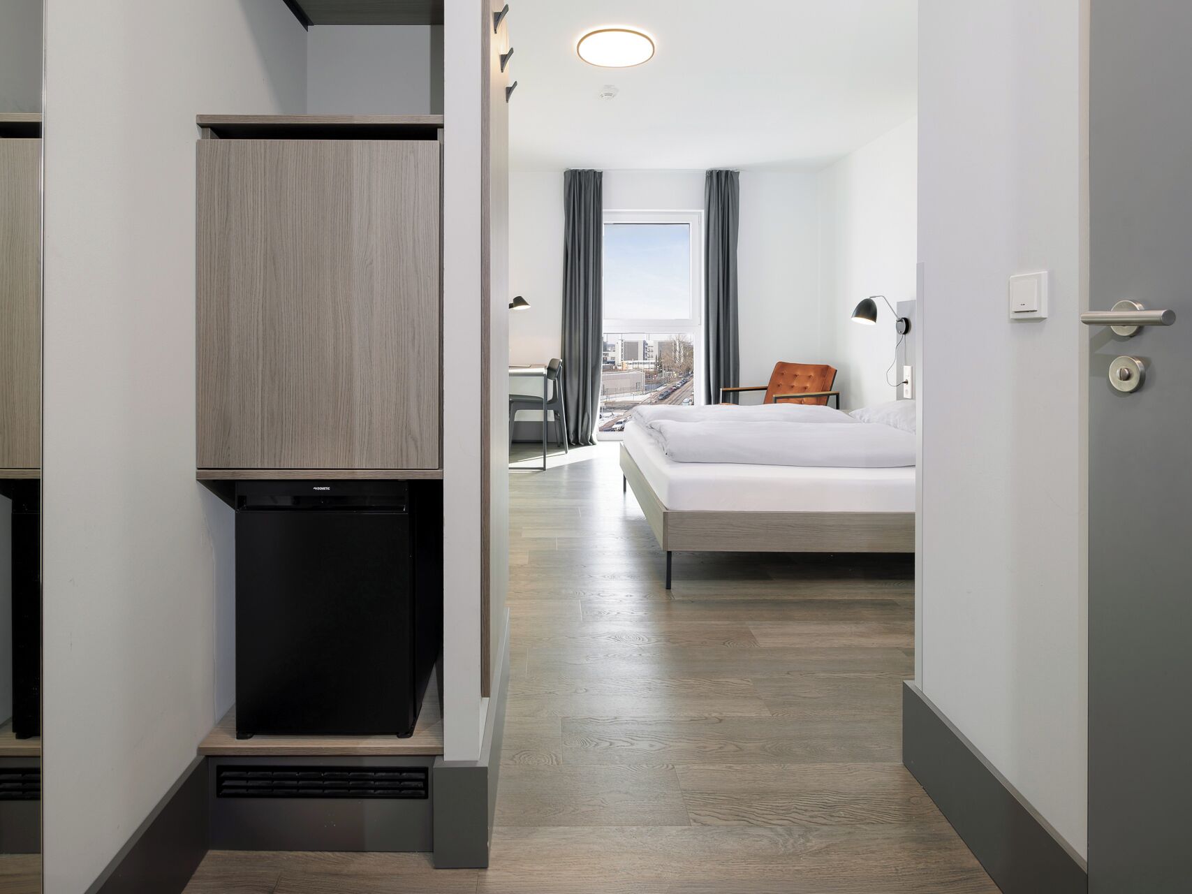 A hotel room with a bed, a desk, and a view of the city.