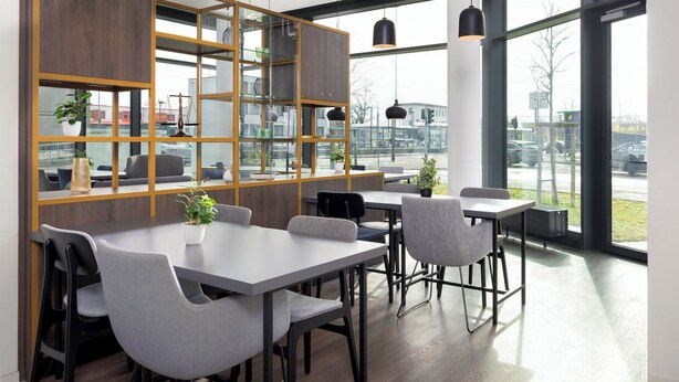 A modern dining area with tables and chairs, large windows, and a view of the street. - smartments Frankfurt City-Ost (Frankfurt)