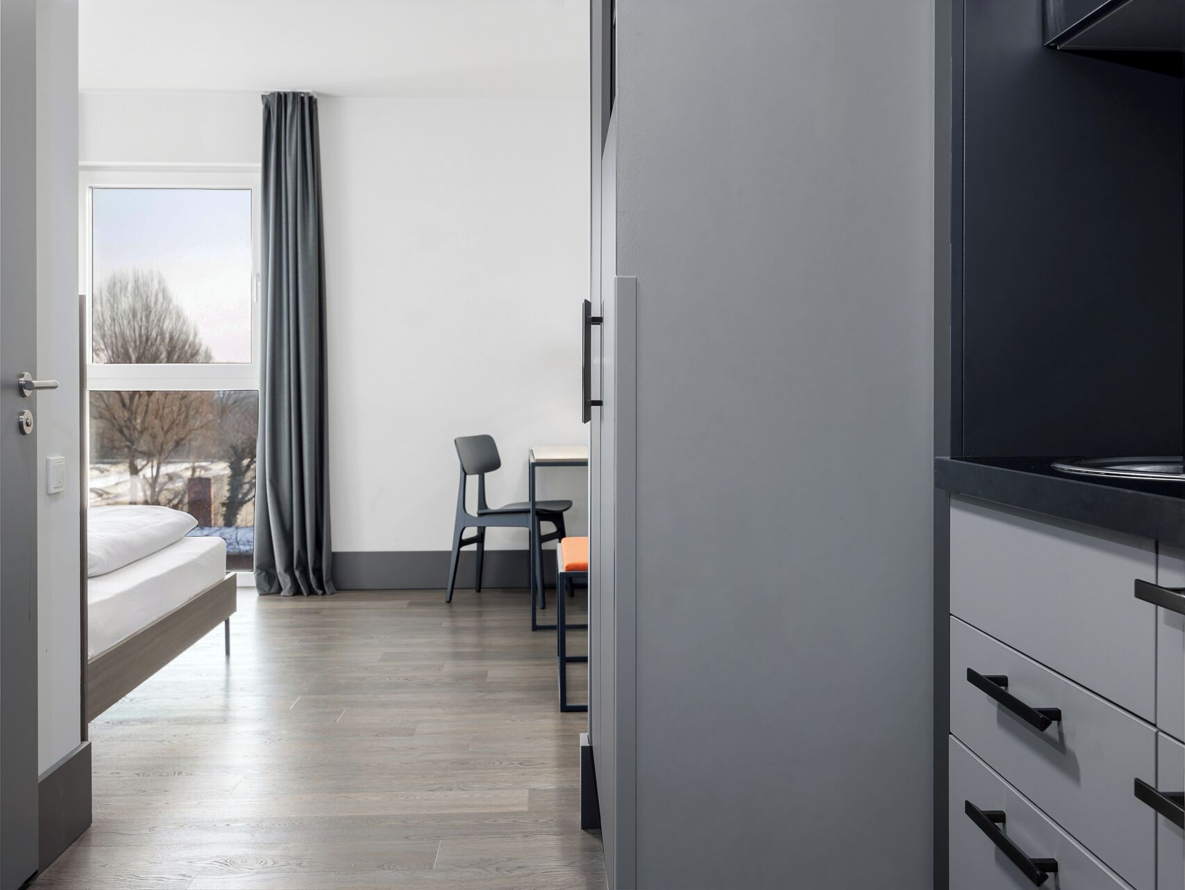 A modern hotel room with a bed, a desk with a chair, a television, and a wardrobe.