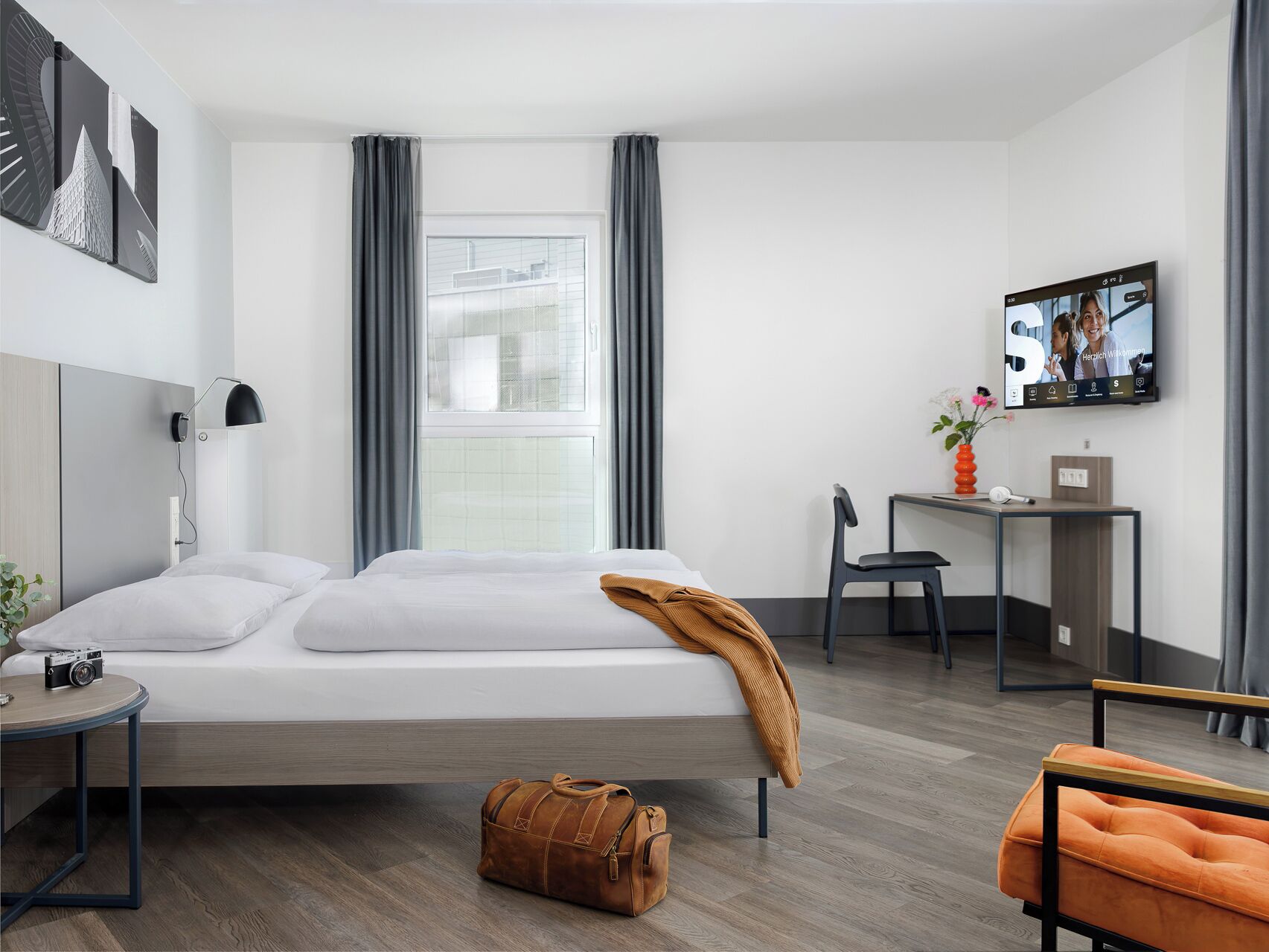 Ett modernt hotellrum med en säng, ett skrivbord, en stol och en tv.