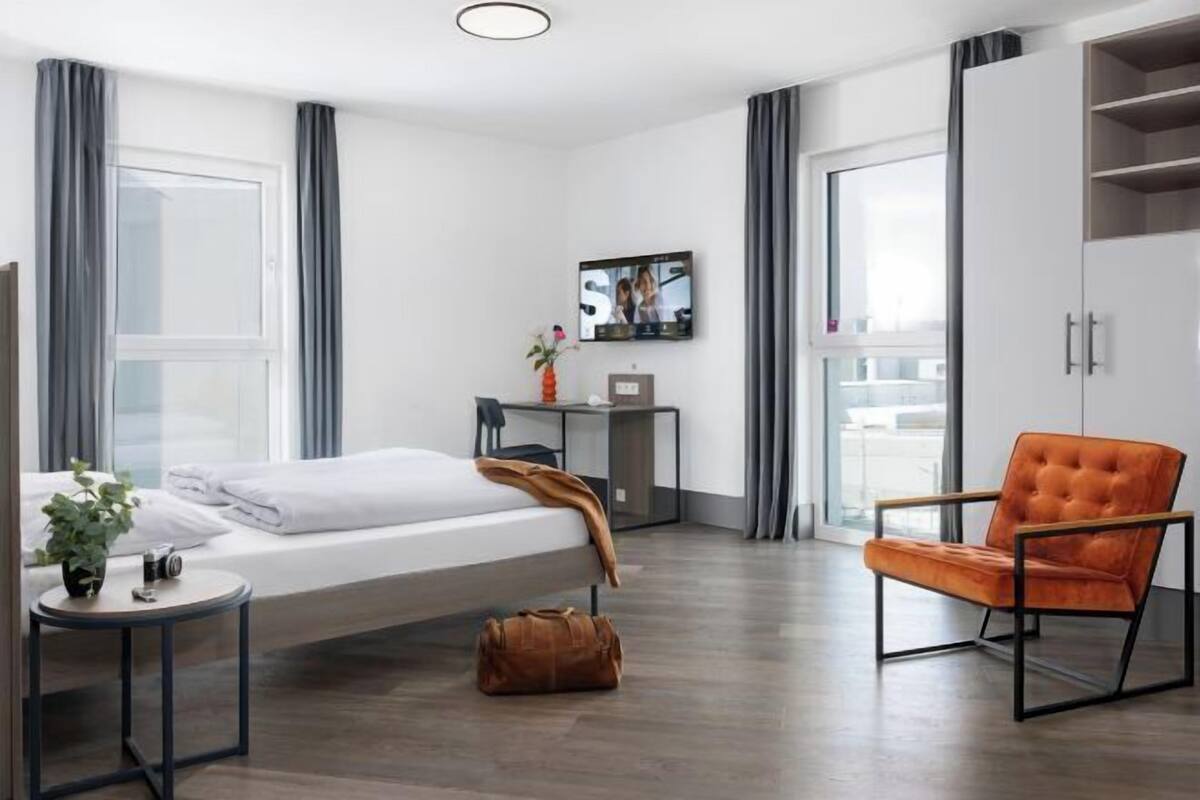 A modern hotel room with a bed, a desk, a TV, and a chair.