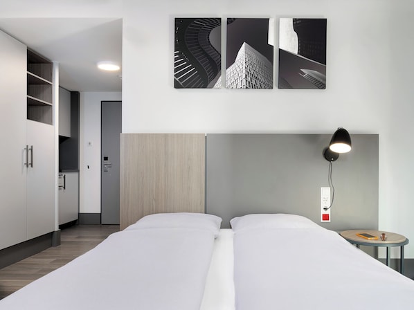 A modern hotel room with a large bed, a desk with a lamp, and a view of a building through the window.