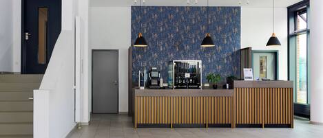 A modern reception area with a wooden reception desk, a coffee machine, and a blue textured wall.