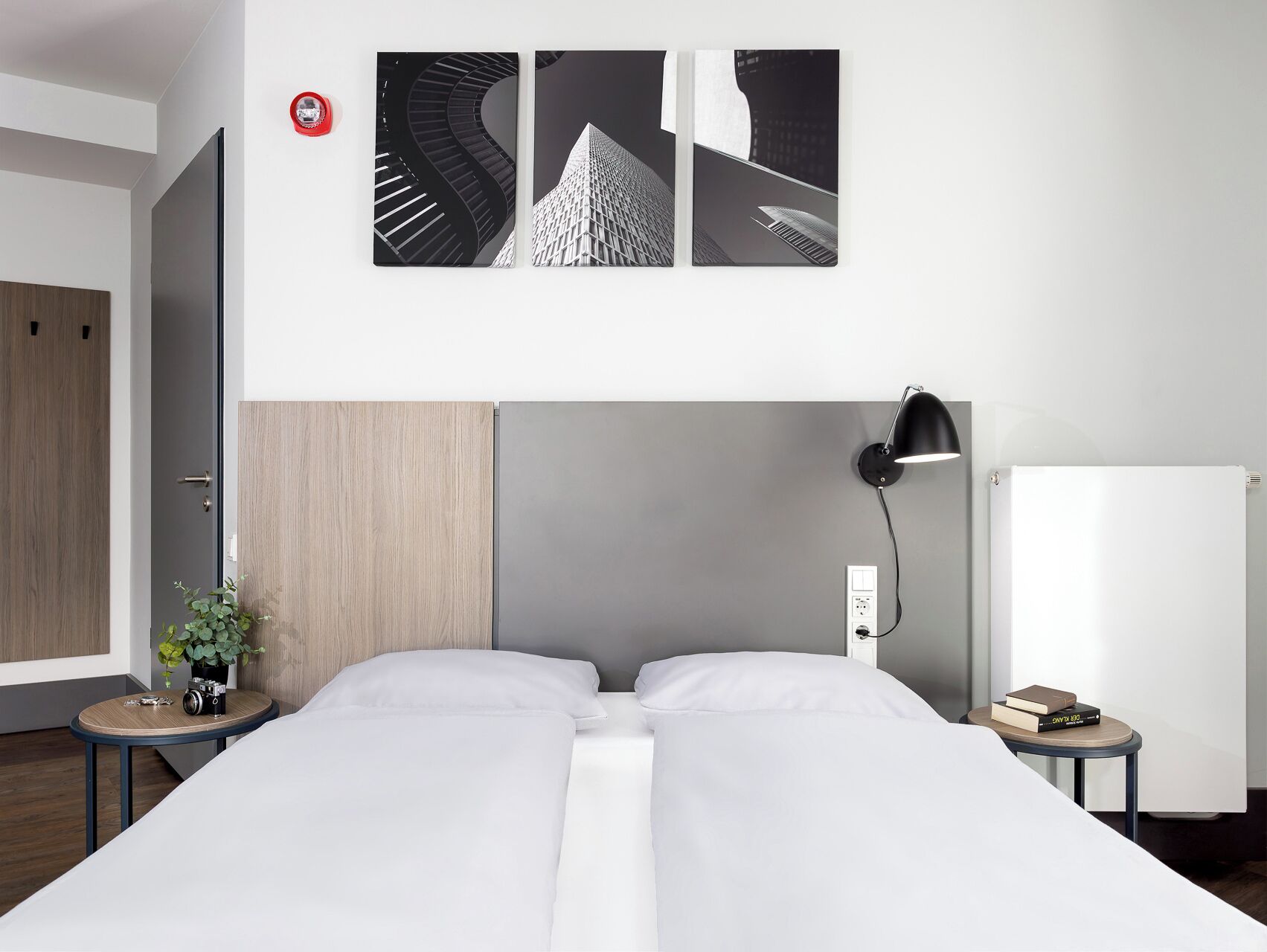 Una habitación de hotel moderna con una cama, una mesita de noche, una lámpara y una obra de arte colgada en la pared.