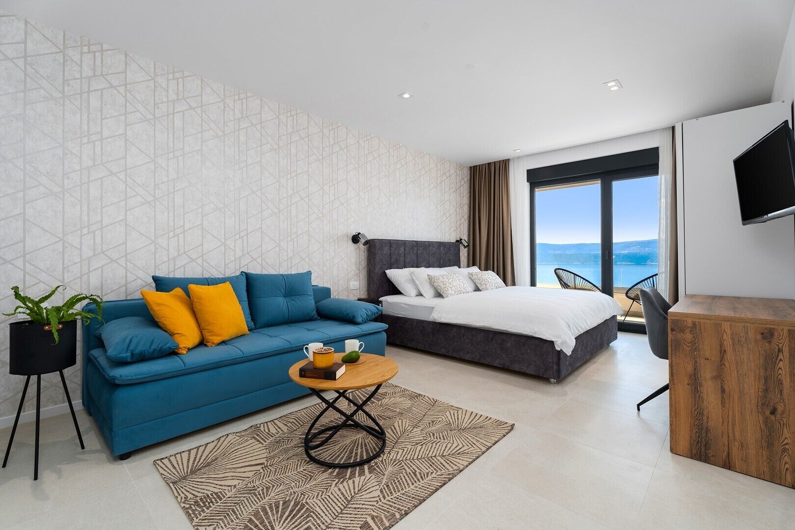 Et moderne hotelværelse med blå sofa, seng, skrivebord og havudsigt.