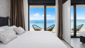 Habitació d'hotel moderna amb un llit gran, dues cadires a prop del balcó i vista al mar.