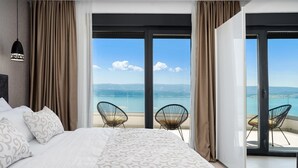 Un dormitori amb un llit gran, dues cadires i vista al mar a través d'una porta corredissa de vidre.
