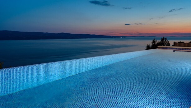 Una piscina infinit que ofereix vistes a una calma extensió d'aigua i muntanyes allunyades durant el crepuscle.
