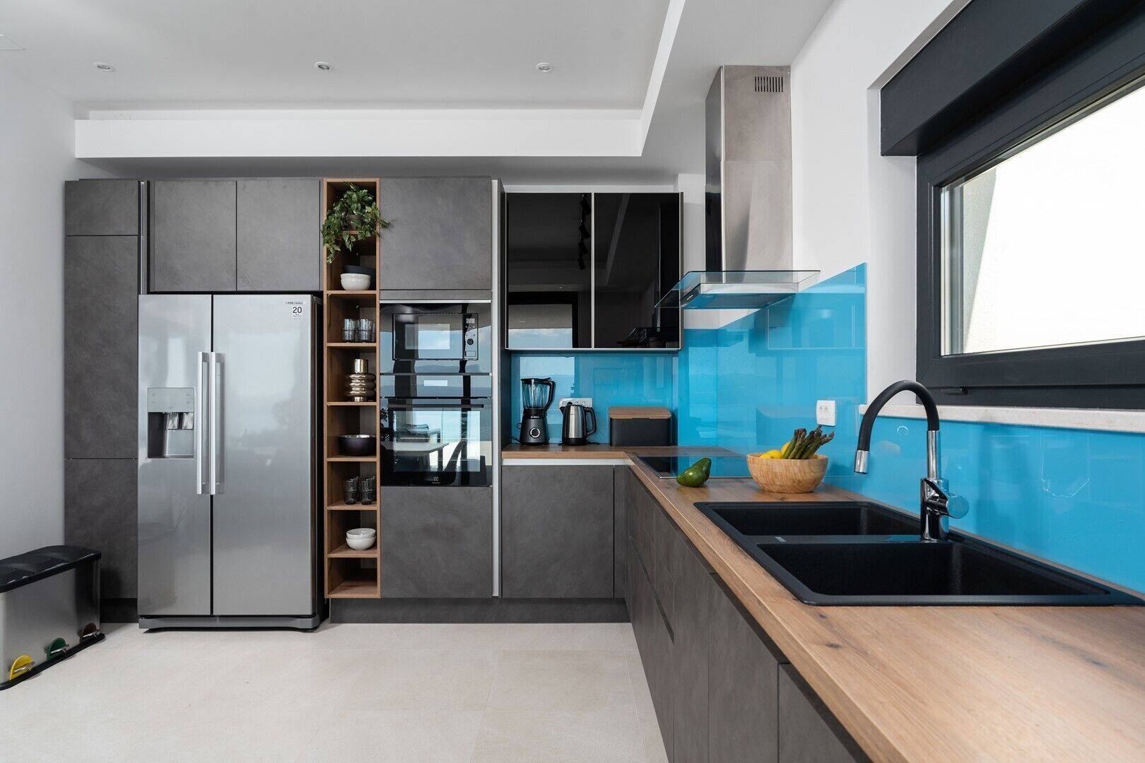 A modern kitchen with a built-in refrigerator, oven, and microwave. There is a sink with a black faucet, a wooden countertop, and a window above the sink.