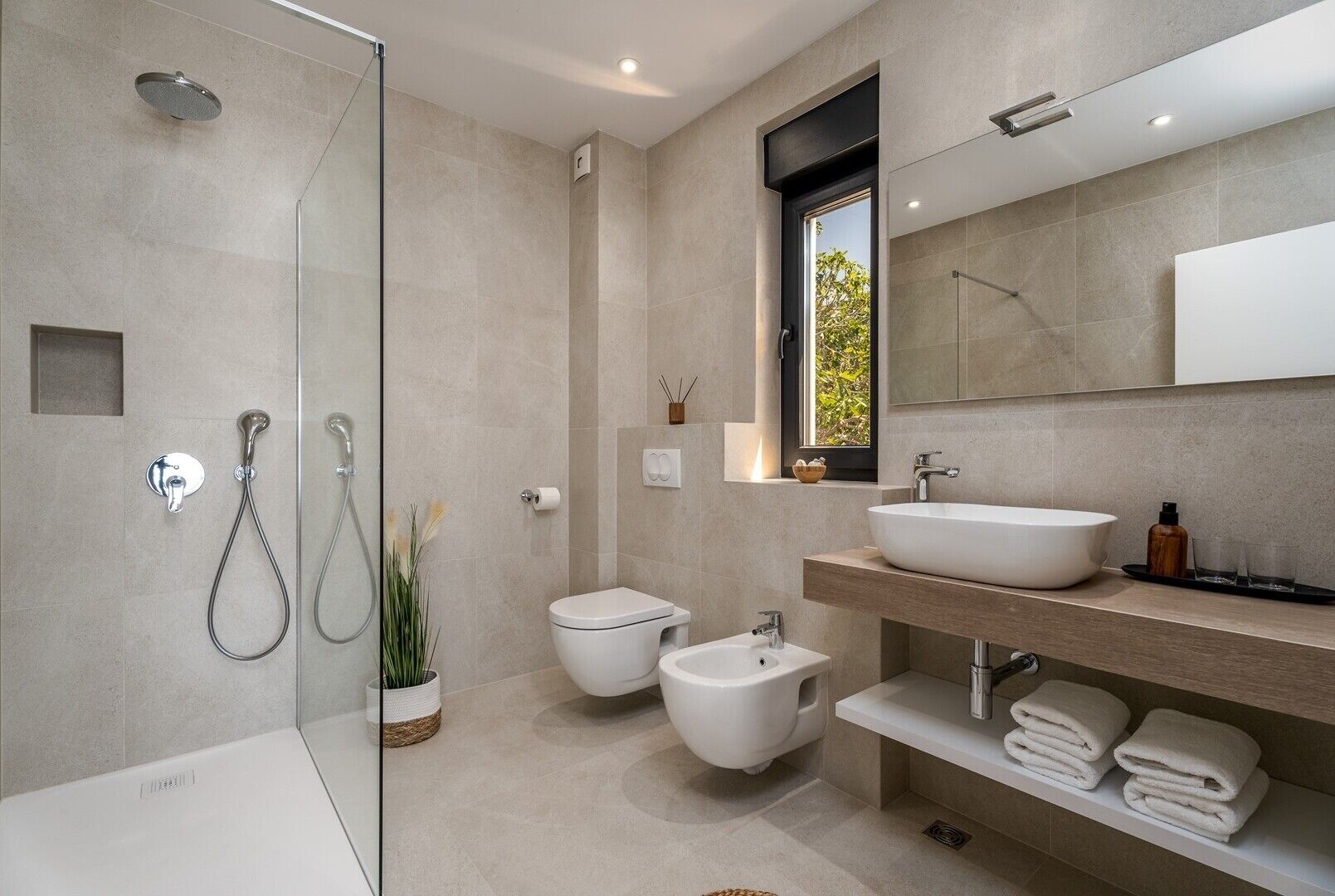 A modern bathroom with a glass-enclosed shower, a bidet, a toilet, a large sink, and a mirror above the sink.