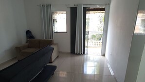 A spacious room with a sofa, a small table, and a sliding glass door leading to an outdoor area. - Lindo APT inteiro mt perto da praia Peró (Cabo Frio)