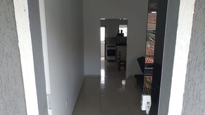 A modern apartment with a tiled floor, a kitchen area visible through an open door, and a small dining area. - Lindo APT inteiro mt perto da praia Peró (Cabo Frio)