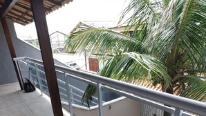 A covered outdoor area with tiled flooring, metal railings, and a view of a residential street with houses and palm trees. - Lindo APT inteiro mt perto da praia Peró (Cabo Frio)