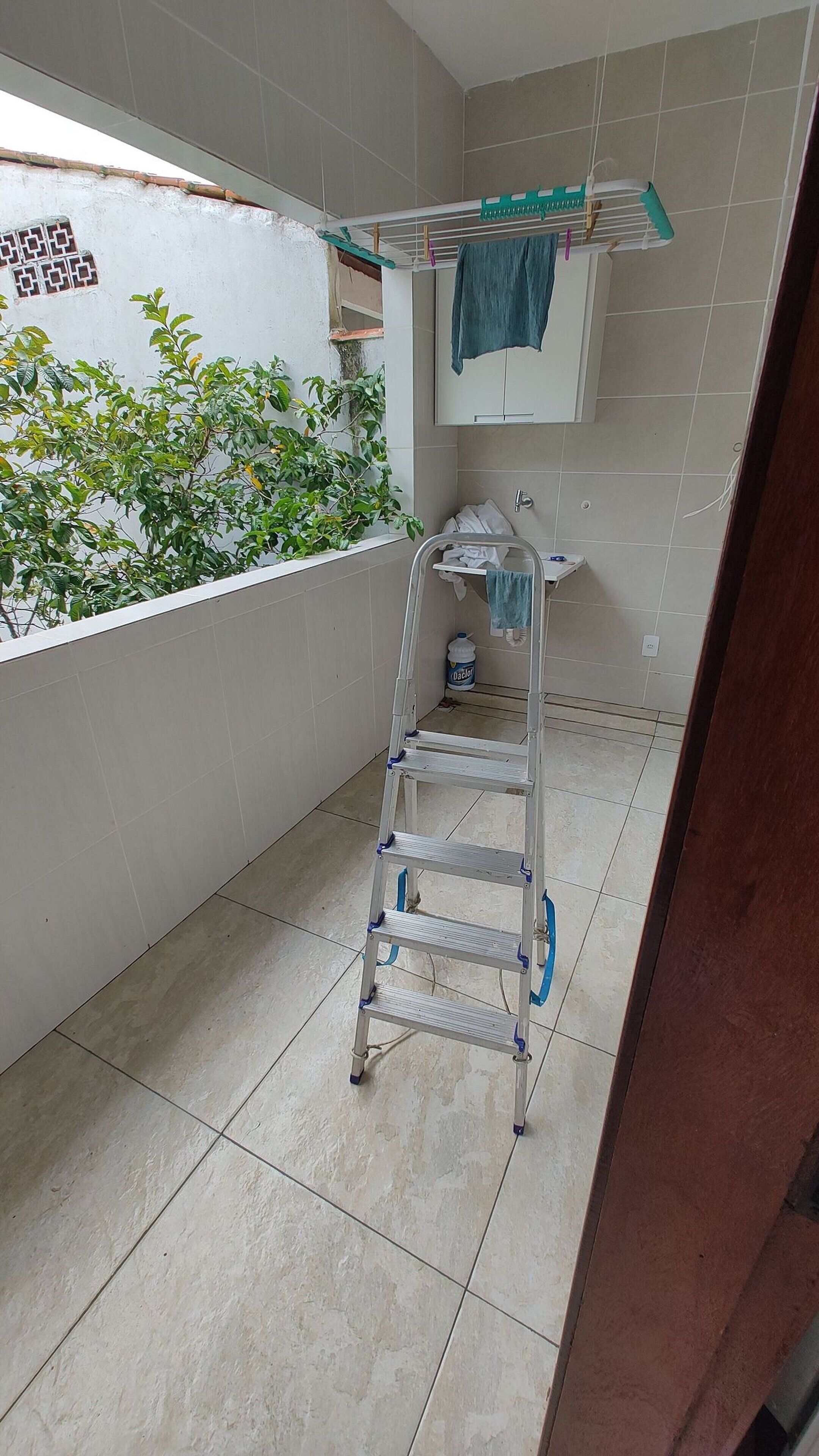 A bathroom with a tiled floor, a metal step ladder, a towel rack, and a window with a view of greenery.