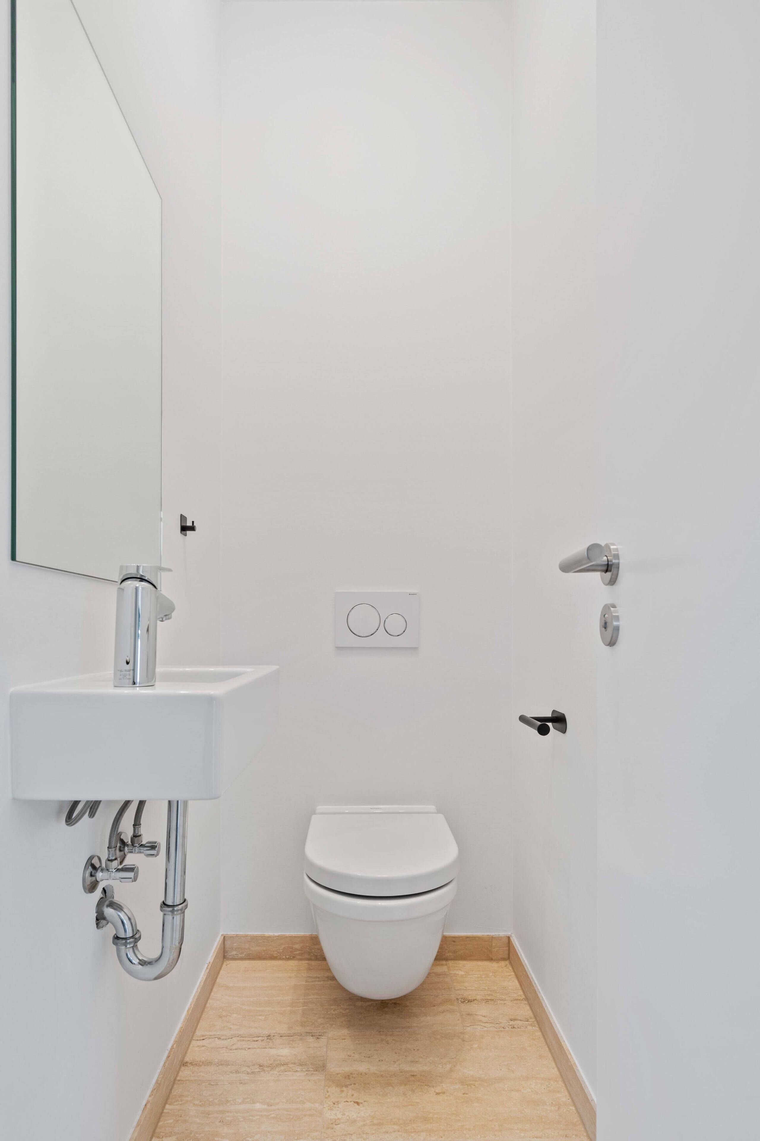 Une petite salle de bain moderne avec des toilettes blanches, un lavabo avec un miroir et une porte de douche.