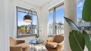 Un soggiorno moderno con due poltrone marroni, un tavolino rotondo, una pianta in vaso e un'ampia finestra che offre vista sugli edifici.