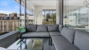 Un balcone moderno con un divano angolare grigio, un tavolino in vetro e vista sulla città.