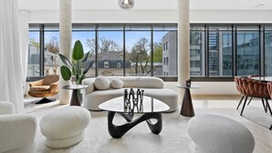 Un soggiorno moderno con un tavolo rotondo in vetro, divani bianchi e un'ampia finestra con vista sulla città.