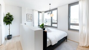 Un dormitorio moderno con cama, ventanas amplias, una planta en maceta y una lámpara colgante.