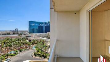 A balcony with a clear view of a cityscape, including a prominent blue building and a landscaped area with palm trees.