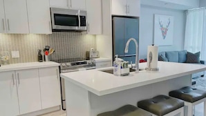 Een moderne keuken met witte kasten, een roestvrijstalen magnetron, een koelkast en een groot eiland met barstoelen.