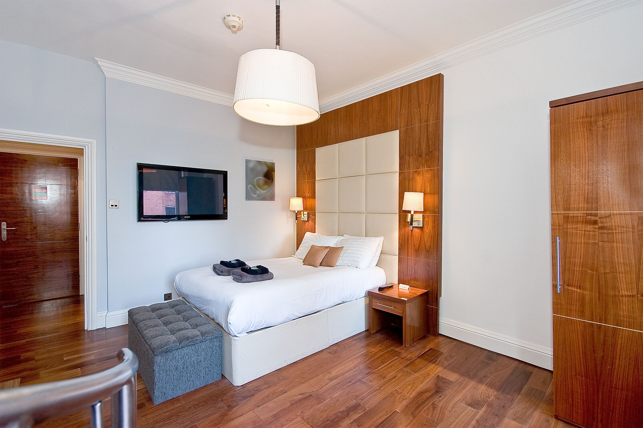 A modern bedroom with a large bed, wooden wardrobe, and a television mounted on the wall.