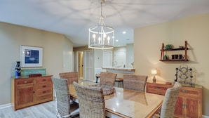 A dining area with a glass-top table, wicker chairs, wooden cabinets, and a chandelier. - Sunset Rentals | Colonnade Club 150 (Hilton Head Island)