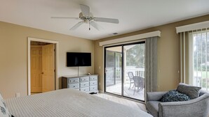 A bedroom with a bed, a dresser, a TV, a ceiling fan, and a sliding glass door leading to a balcony. - Sunset Rentals | Colonnade Club 150 (Hilton Head Island)