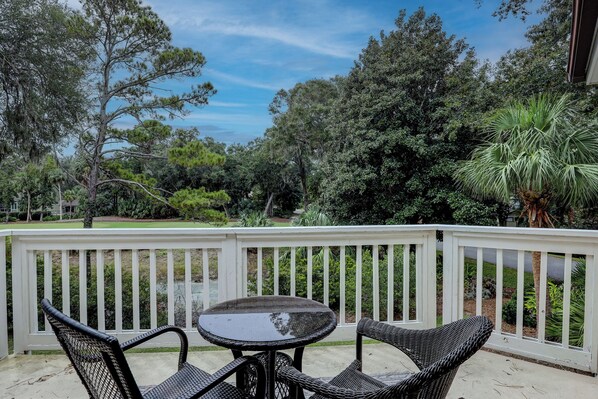 An outdoor patio with a round table and two wicker chairs, surrounded by a white railing. - Sunset Rentals | Colonnade Club 150 (Hilton Head Island)