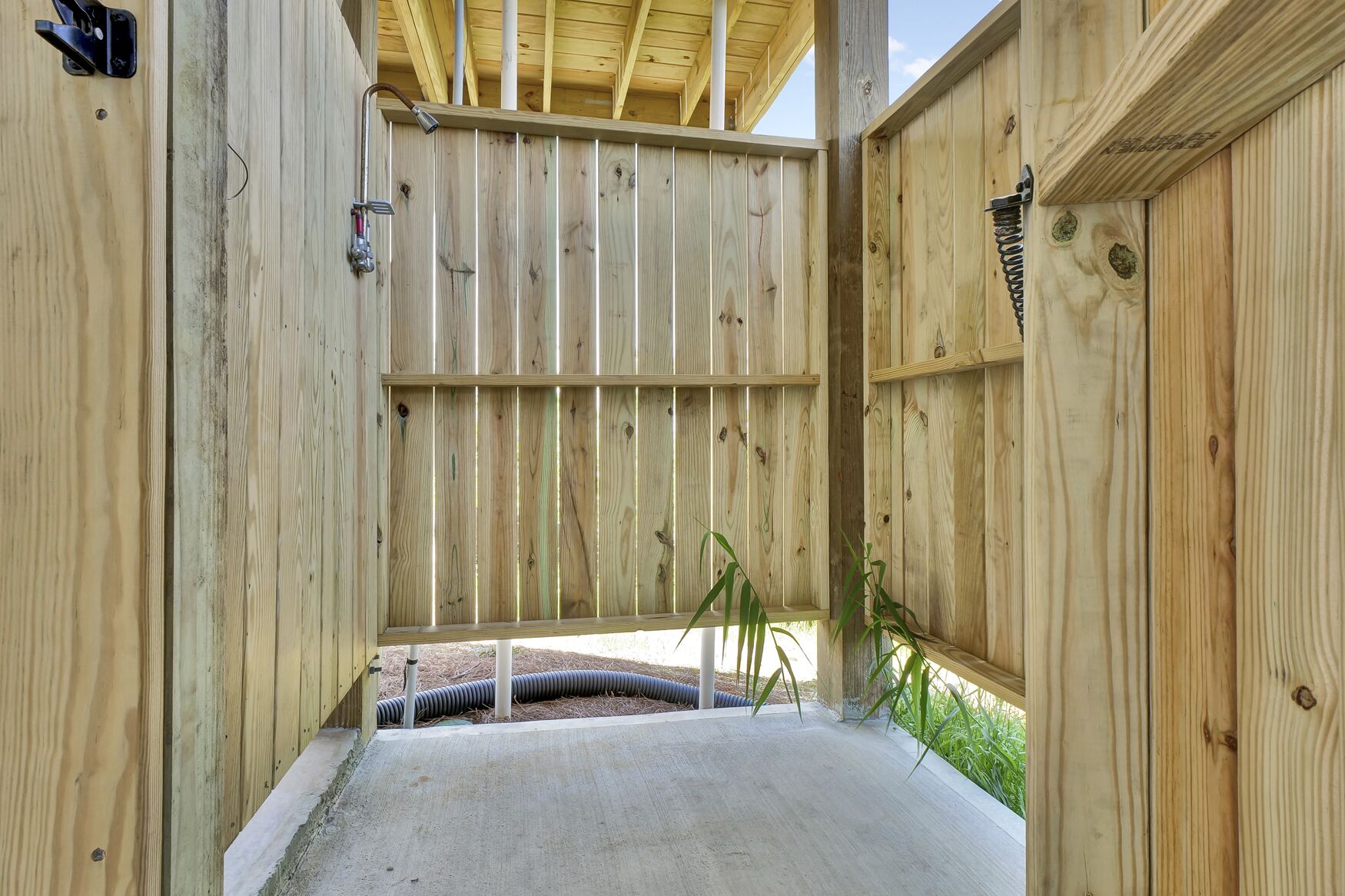 A wooden deck with a concrete floor, metal railings, and a hose running along the wall.