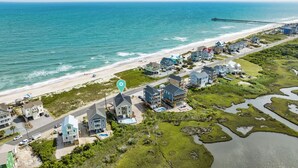 Vue aérienne d’une zone résidentielle côtière, avec des maisons, une plage et une jetée.