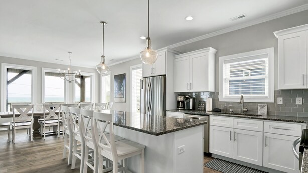 Une cuisine moderne avec des meubles blancs, des plans de travail en granit et des luminaires suspendus.