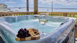 Un bain à remous avec une terrasse en bois, un verre de vin blanc et un assortiment de fromages et de fruits.