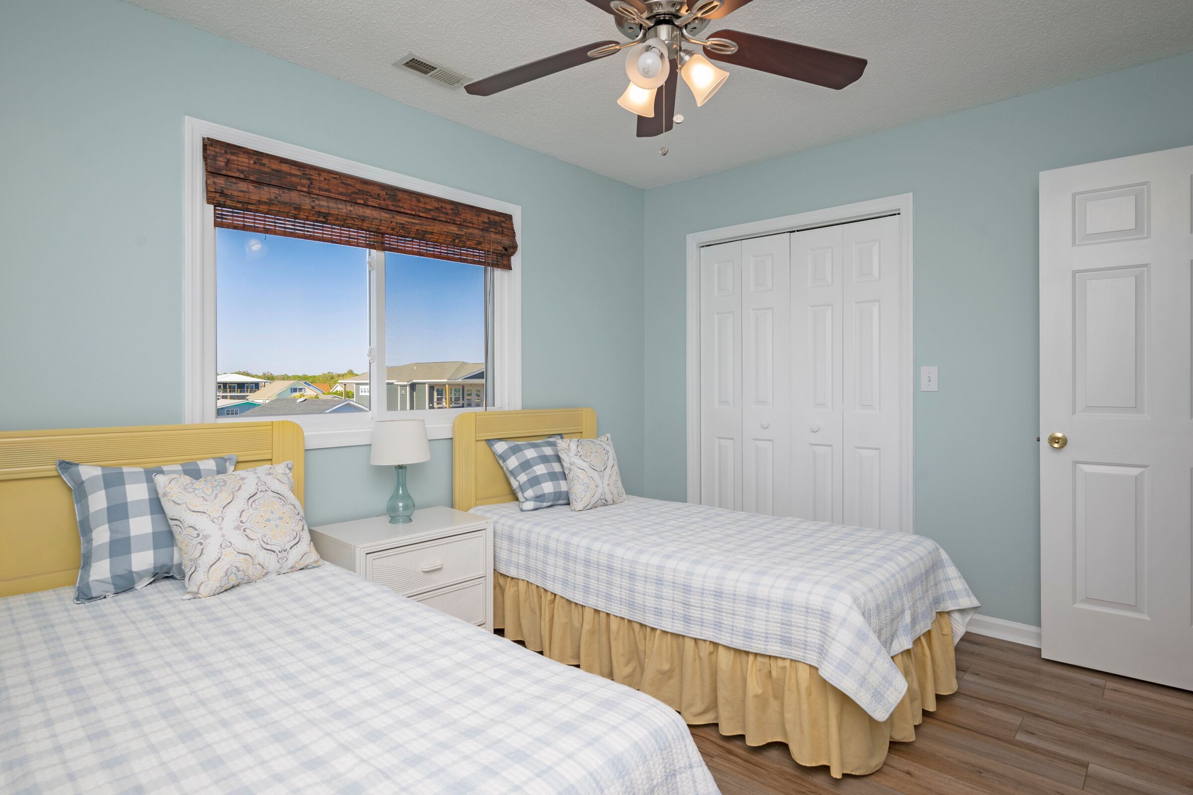 A bedroom with two beds, a ceiling fan, a window with a view, and a door.