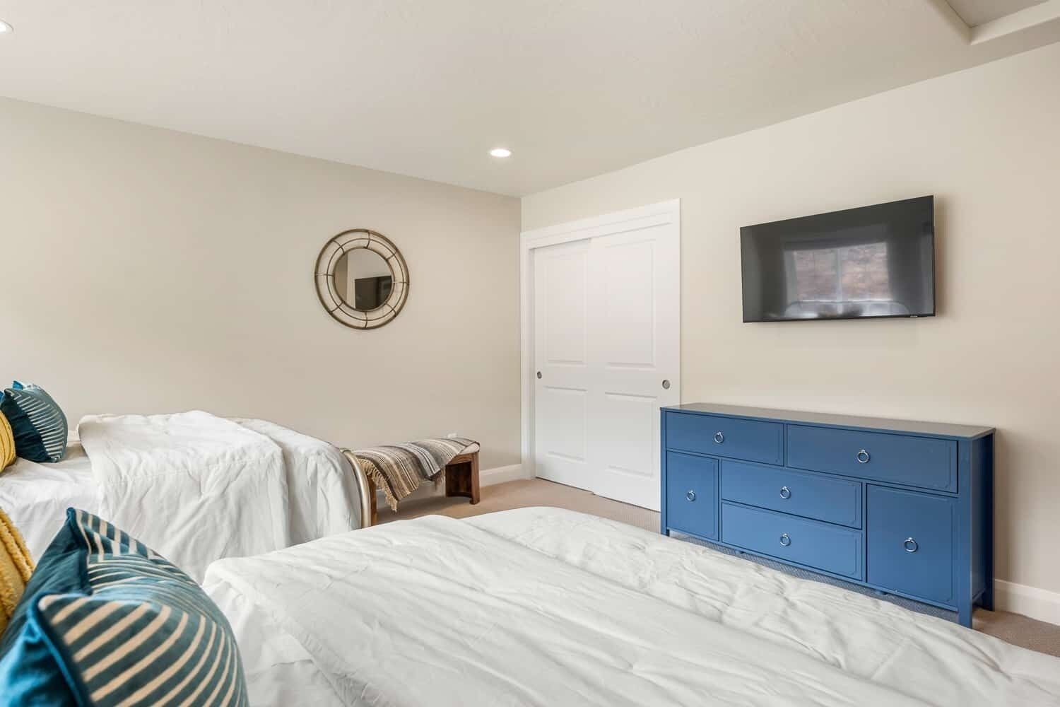 A bedroom with two beds, a blue dresser, a mirror, and a door.