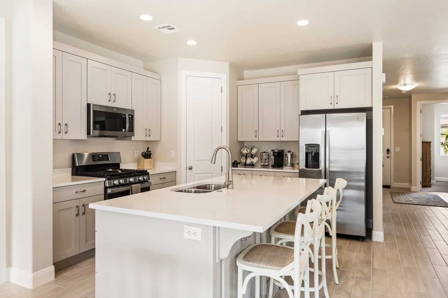 A modern kitchen with white cabinetry, stainless steel appliances, and a central island with bar stools.