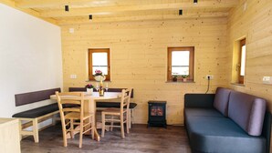 Un interior de cabaña acogedor, con una mesa de comedor de madera, bancos, un sofá y un estufa de leña.