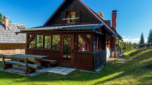 A rustic cabin with a large deck, a picnic table, and a chimney.
