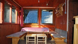 A wooden cabin with a bench seating area, a table, and a view of a blue-roofed building outside.